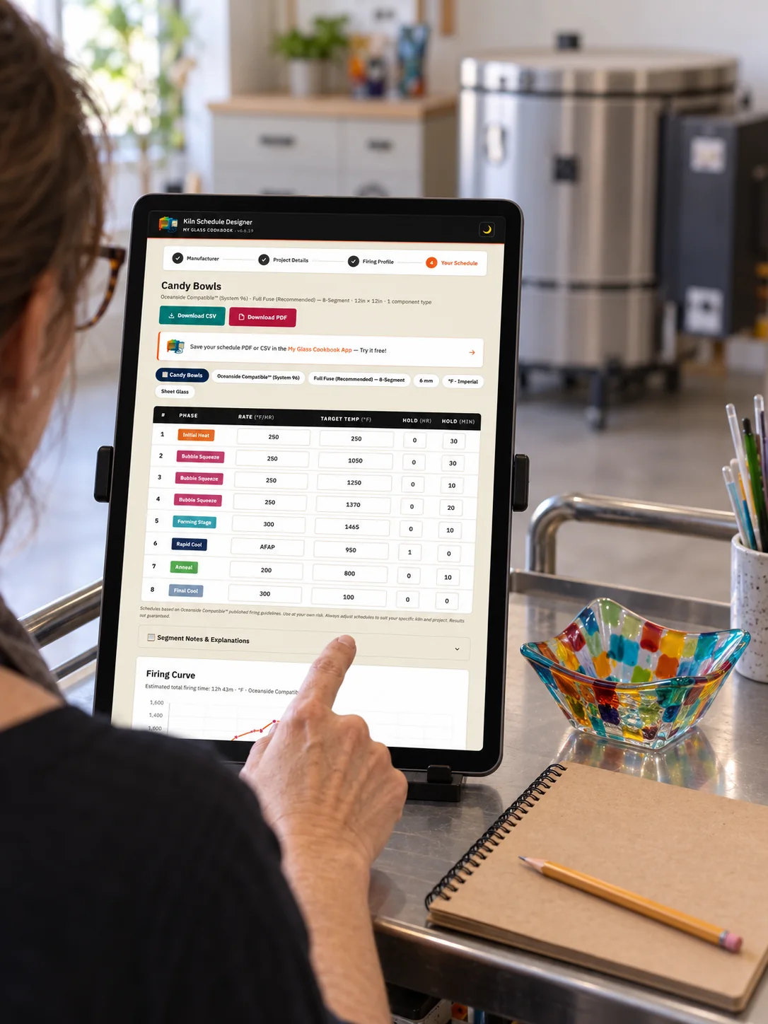 Kiln Schedule Designer on a portrait tablet beside a finished glass bowl and closed kiln