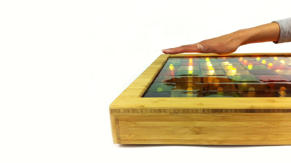 A hand hovering over the glass surface of a bamboo-framed Umbra light object on white