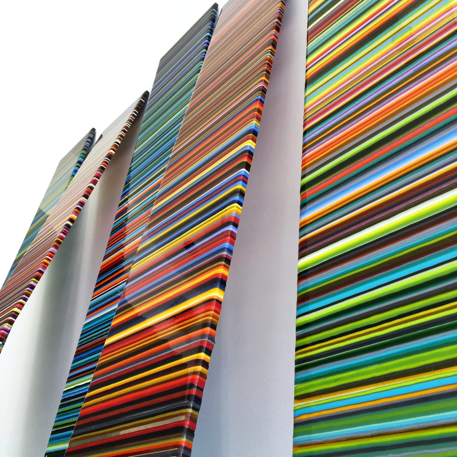 Five tall multicoloured striped glass panels leaning against a white wall